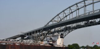Cargo ship passing under the Blue Water Bridge connecting USA and Canada on a clear day.