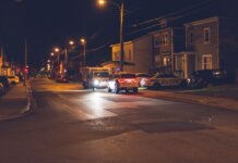 Полиция Гамильтона ищет троих подозреваемых в вооружённом вторжении в жилой дом Cars with glowing lights parked on asphalt road near police car placed near residential building in small town in evening