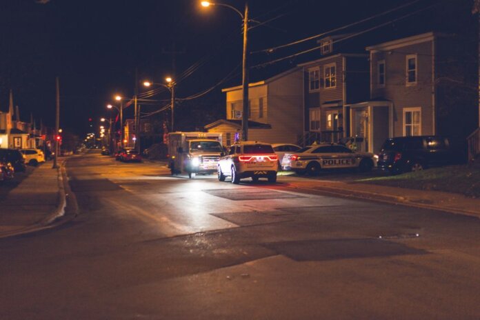Cars with glowing lights parked on asphalt road near police car placed near residential building in small town in evening Cars with glowing lights parked on asphalt road near police car placed near residential building in small town in evening