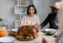 Cheerful multiethnic people having dinner together at table with roasted turkey while celebrating Thanksgiving Day