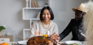 Cheerful multiethnic people having dinner together at table with roasted turkey while celebrating Thanksgiving Day