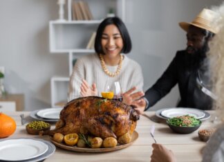Cheerful multiethnic people having dinner together at table with roasted turkey while celebrating Thanksgiving Day