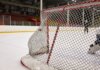 Close-up of a hockey goal on an indoor rink with players practicing in the background.