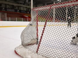 Close-up of a hockey goal on an indoor rink with players practicing in the background.