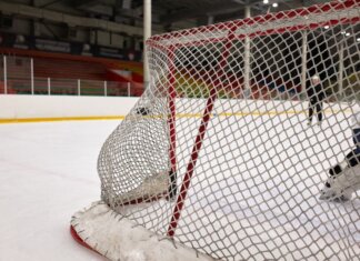 Close-up of a hockey goal on an indoor rink with players practicing in the background.