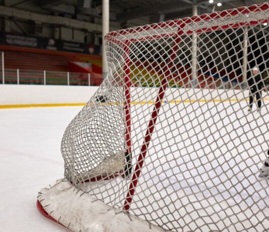 Close-up of a hockey goal on an indoor rink with players practicing in the background.