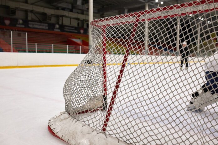 Close-up of a hockey goal on an indoor rink with players practicing in the background. Close-up of a hockey goal on an indoor rink with players practicing in the background.