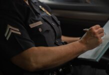 В Калгари двоим предъявлены обвинения в мошенничестве на $1 млн Close-up of a police officer writing in a notebook while sitting in a car, focused detail.