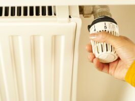 Close-up of hand adjusting radiator thermostat to control home heating temperature.