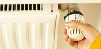 Close-up of hand adjusting radiator thermostat to control home heating temperature.