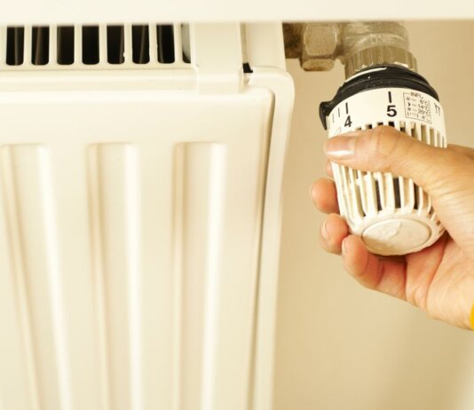 Close-up of hand adjusting radiator thermostat to control home heating temperature.