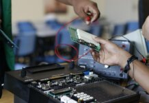 Close-up of hands working with electronics equipment and circuit board in a lab setting.