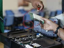 Close-up of hands working with electronics equipment and circuit board in a lab setting.