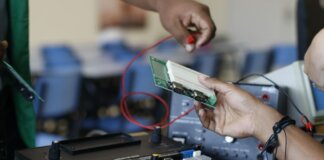 Close-up of hands working with electronics equipment and circuit board in a lab setting.