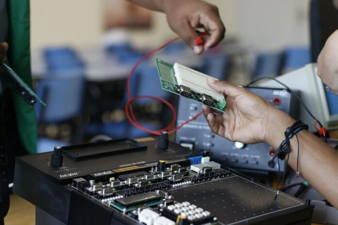 Close-up of hands working with electronics equipment and circuit board in a lab setting. Close-up of hands working with electronics equipment and circuit board in a lab setting.