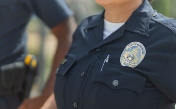 Close-up of police officers in uniform, displaying badge and radio outdoors.