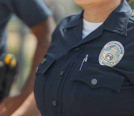 Close-up of police officers in uniform, displaying badge and radio outdoors.