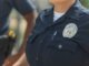Close-up of police officers in uniform, displaying badge and radio outdoors.