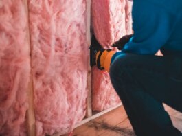 Crop unrecognizable worker in gloves sitting on haunches and insulating with pink stone wool