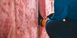 Crop unrecognizable worker in gloves sitting on haunches and insulating with pink stone wool