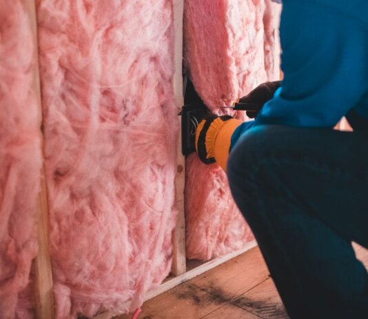 Crop unrecognizable worker in gloves sitting on haunches and insulating with pink stone wool
