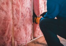 Crop unrecognizable worker in gloves sitting on haunches and insulating with pink stone wool
