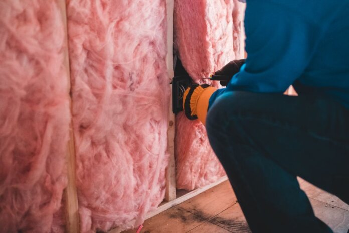 Crop unrecognizable worker in gloves sitting on haunches and insulating with pink stone wool Crop unrecognizable worker in gloves sitting on haunches and insulating with pink stone wool