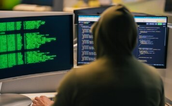 Хакер в капюшоне за несколькими мониторами