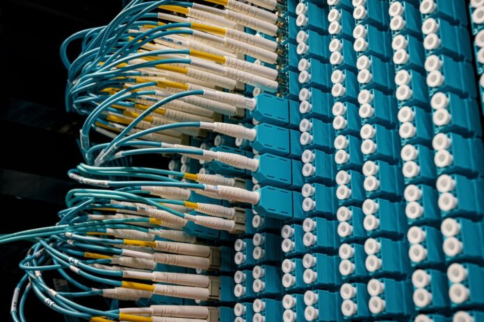 Detailed view of fiber optic patch cables connecting to a blue patch panel in a data center. Detailed view of fiber optic patch cables connecting to a blue patch panel in a data center.