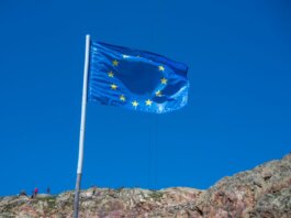 European Union flag waving atop a rocky hill with clear blue sky backdrop.