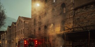 Firefighters managing smoke outside a historic building at dusk. Urban emergency response in action.