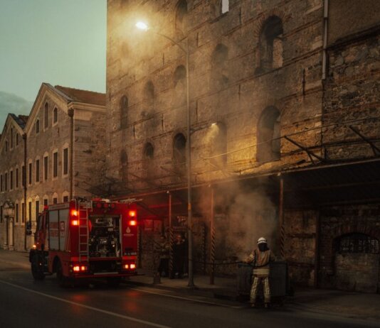 Firefighters managing smoke outside a historic building at dusk. Urban emergency response in action.