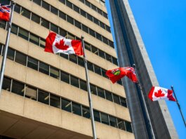 Flags of Canada and Ontario fluttering near the CN Tower under a clear blue sky in Toronto.