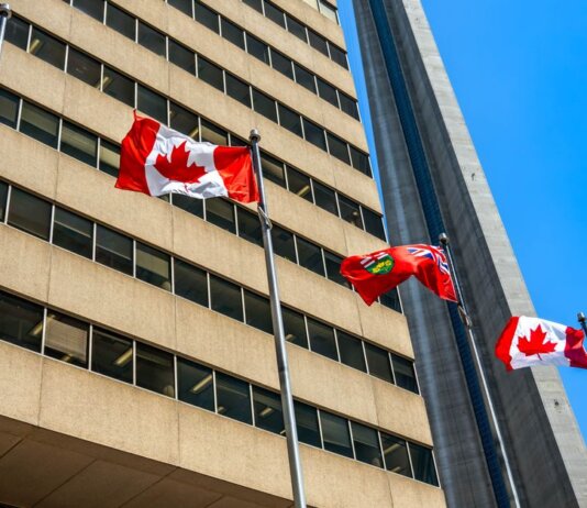 Flags of Canada and Ontario fluttering near the CN Tower under a clear blue sky in Toronto.
