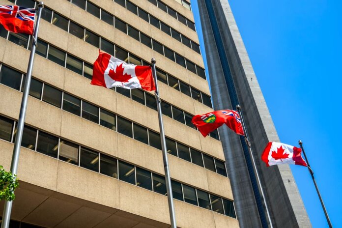 Flags of Canada and Ontario fluttering near the CN Tower under a clear blue sky in Toronto.