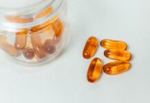 Glass container with amber capsules spilling out on a white background.