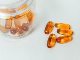 Glass container with amber capsules spilling out on a white background.