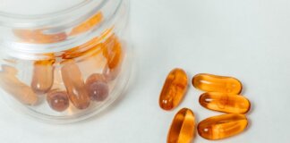 Glass container with amber capsules spilling out on a white background.