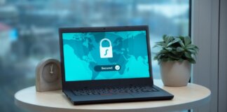 Laptop displaying a security lock icon on a table with a potted plant and clock.