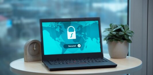 Laptop displaying a security lock icon on a table with a potted plant and clock.