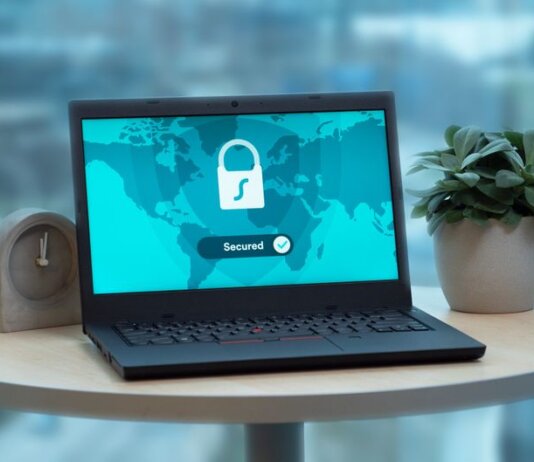 Laptop displaying a security lock icon on a table with a potted plant and clock.