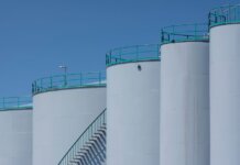 Large industrial storage tanks with green railings against a clear blue sky.