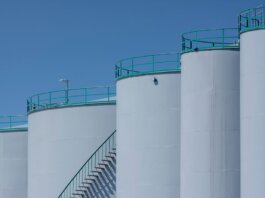 Large industrial storage tanks with green railings against a clear blue sky.