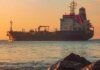Large oil tanker on the ocean near the coast, sailing under a vibrant sunset sky.