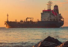 Large oil tanker on the ocean near the coast, sailing under a vibrant sunset sky.