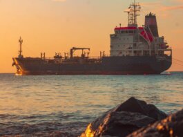 Large oil tanker on the ocean near the coast, sailing under a vibrant sunset sky.