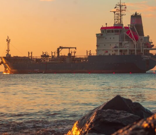 Large oil tanker on the ocean near the coast, sailing under a vibrant sunset sky.