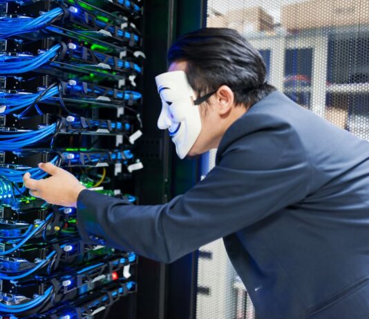 Masked individual interacting with server racks, symbolizing cybersecurity threats.
