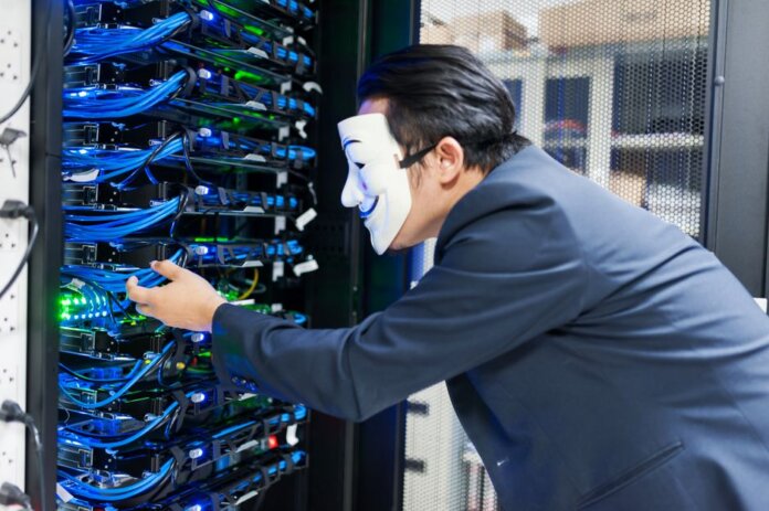 Masked individual interacting with server racks, symbolizing cybersecurity threats. Masked individual interacting with server racks, symbolizing cybersecurity threats.