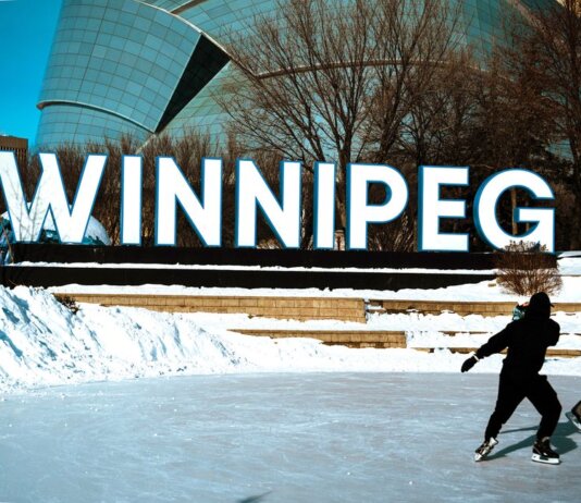 People ice skating in front of the iconic Winnipeg sign on a sunny winter day.